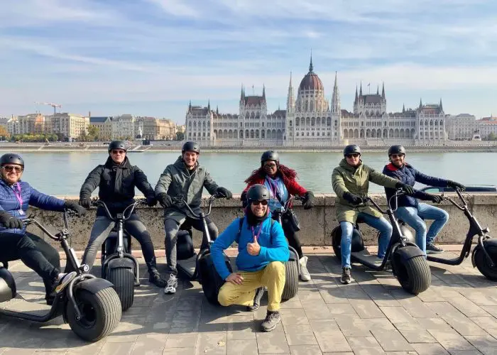 People on an e-scooter tour posing with the Parliament in the background.