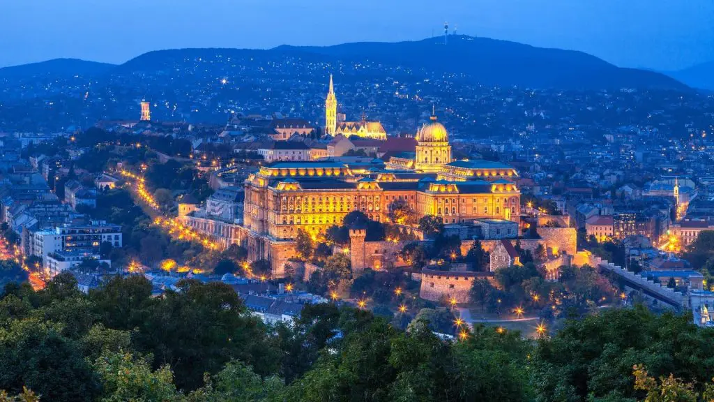 Night view of Budapest, featuring the illuminated Buda Castle and surrounding historic buildings with the cityscape and distant hills in the background—a perfect backdrop for your Budapest stag do ideas.