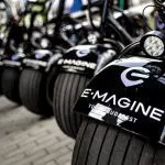 A row of black electric scooters with 'E-MAGINE TOURS BUDAPEST' logos are parked on a tiled ground, showing where and how to rent an electric scooter in Budapest.