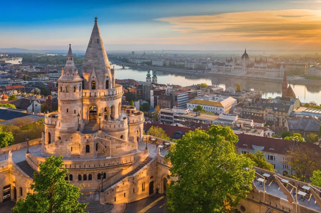 Aerial view of Fisherman's Bastion in Budapest, Hungary with the Danube River and Hungarian Parliament Building in the background during sunset.