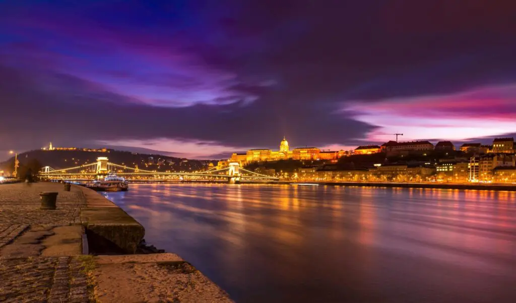 Nighttime view of Budapest’s Chain Bridge and Buda Castle illuminated along the Danube River, with a vibrant purple and blue sky—an iconic Budapest at night scene featured in every top Budapest guide.