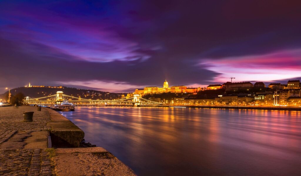 Nighttime view of Budapest’s Chain Bridge and Buda Castle illuminated along the Danube River, with a vibrant purple and blue sky—an iconic Budapest at night scene featured in every top Budapest guide.