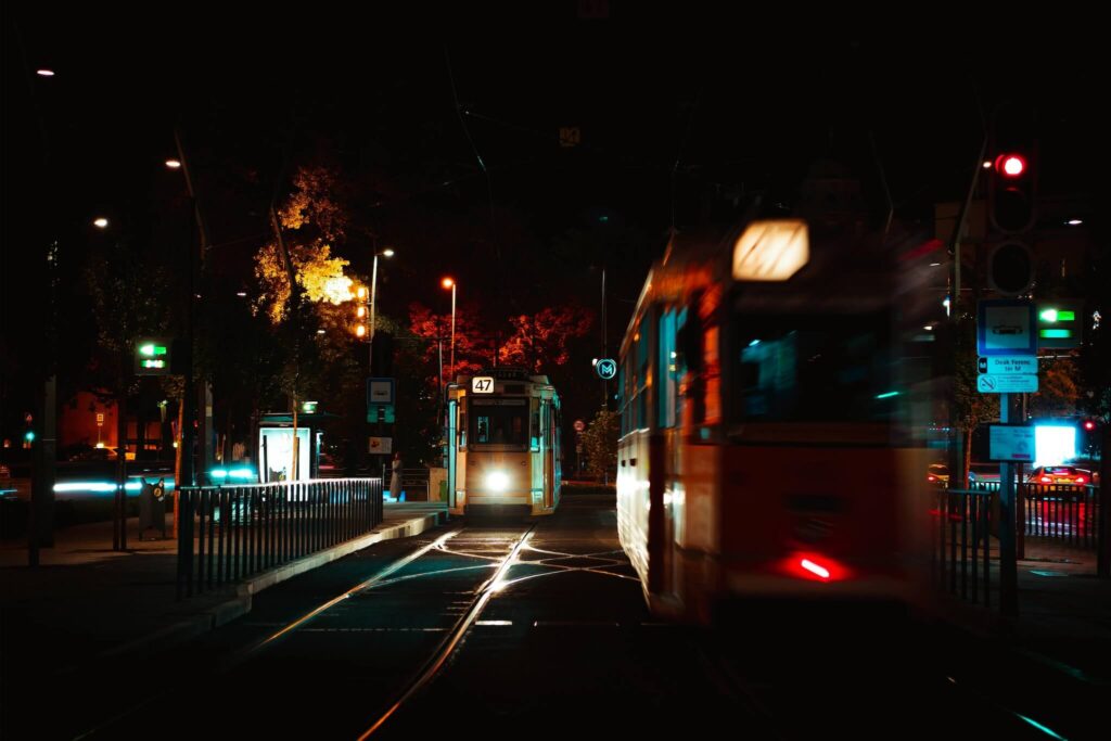 Two trams pass each other at night on city tracks, illuminated by streetlights and traffic signals. The blurred motion captures the vibrant urban atmosphere of Budapest at night—a must-see scene for any Budapest guide.