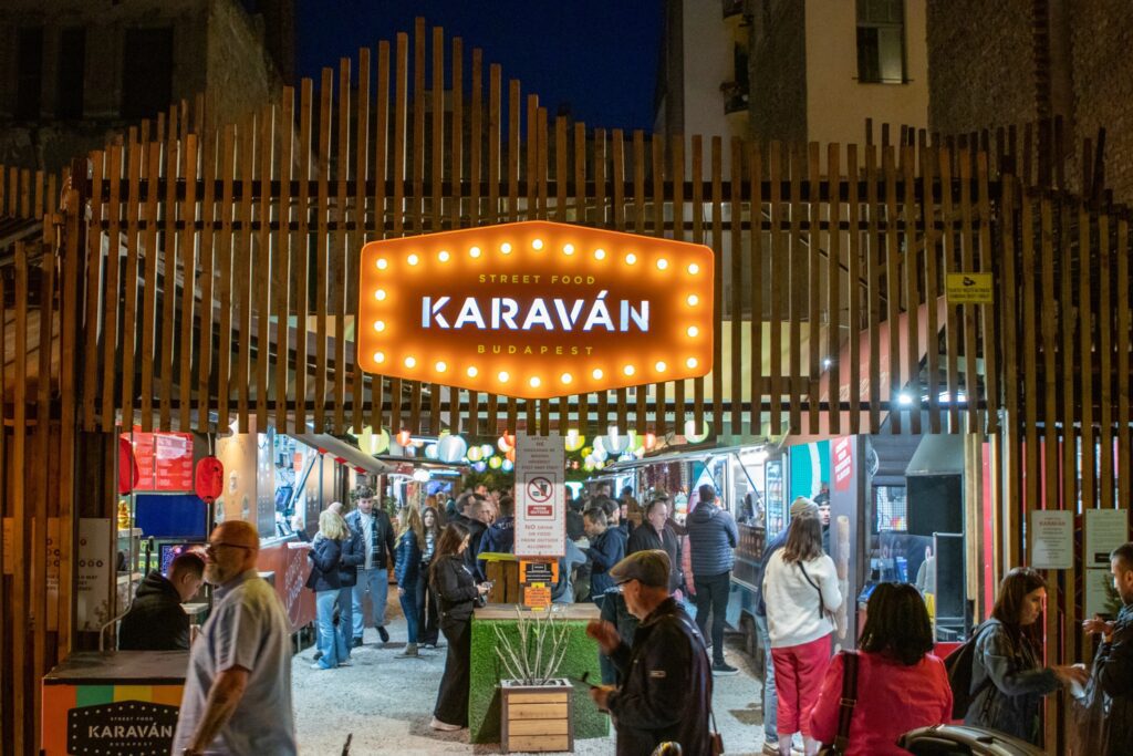 People gather at night under a brightly lit Karaván Street Food Budapest sign, entering a lively outdoor food market—a must-see for any Budapest guide and one of the best things to do in Budapest at night.
